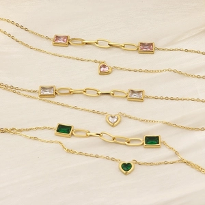 Detail of layered gold bracelets featuring heart charms and colorful square zircons