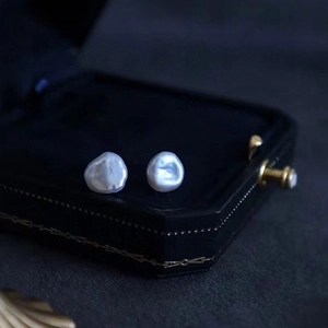 Macro shot of Baroque pearl stud earrings resting on a vintage black jewelry box