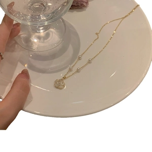 Elegant gold flower necklace with pearls and hollow floral pendant on ceramic tray