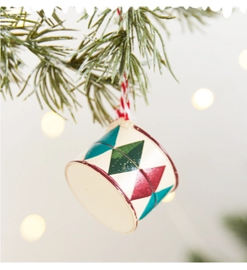 Close-up of a festive painted drum ornament hanging on a pine tree with bokeh lights