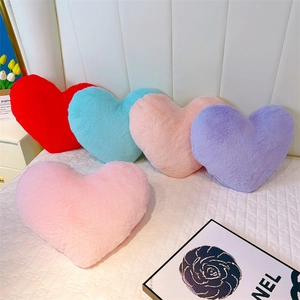 Détails des coussins peluche cœur moelleux en rose et violet sur un lit douillet