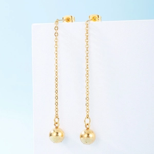 Détail d'une boucle d'oreille longue chaîne dorée avec pendentif boule sur support blanc