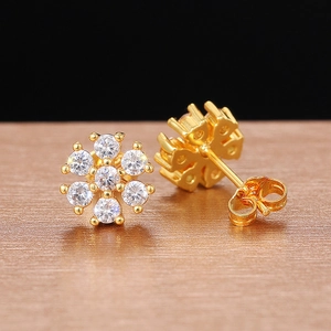 Close-up of golden flower stud earrings with clear zircon stones on a bronze surface