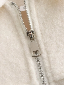 Detail of light beige faux shearling jacket with smooth metal zipper and plush texture