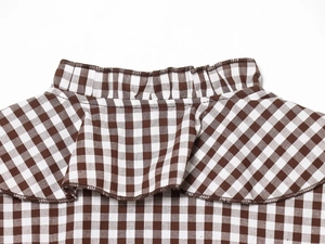 Détail du col à volants d'une chemise en coton à carreaux marron et blanc