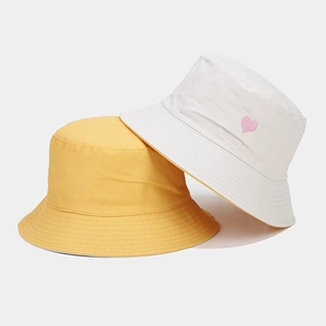 Détail de bobs réversibles jaune et beige avec broderie cœur et texture en coton dense