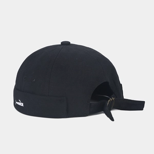 Close-up of black brimless cap featuring a white whale embroidery and bronze metal buckle