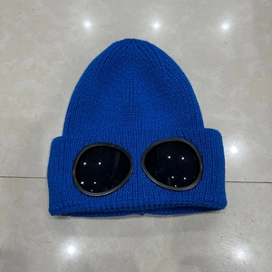 Flat lay of royal blue knit beanie with integrated black goggles on marble tile