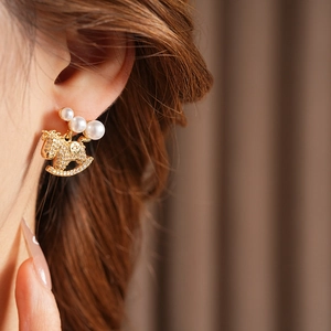 Détail d'une boucle d'oreille cheval à bascule dorée avec perles sur un modèle