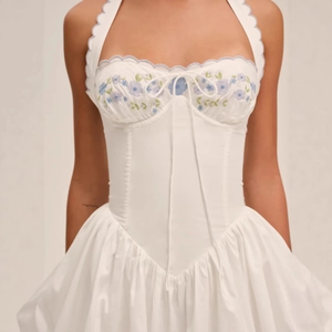 White halter neck dress with blue floral embroidery and pleated corset design bodice