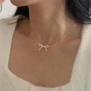 Close-up of golden bow-shaped pearl pendant necklace worn on a white sweater
