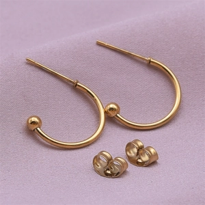Detail of C-shaped gold-plated stainless steel earrings with ball ends on purple fabric