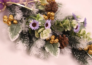 Detail of Christmas wreath with frosted pine needles, golden berries and purple daisies