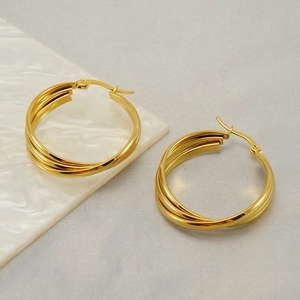 Polished gold multi-layer hoop earrings with triple interlocking rings on modern textured background