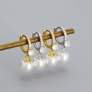 Detail of gold and silver pearl earrings with zircon inlay hanging on a metal rod