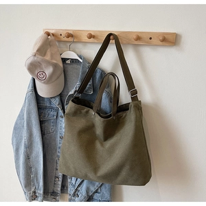 Detail of dark green canvas tote bag with dual handles hanging on a wooden wall hook