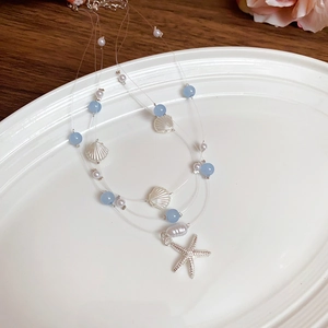 Multi-layer necklace with blue beads, pearls, silver shells and starfish on white plate