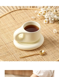 Creamy ceramic fat mug and saucer set with rounded handle and gold spoon in warm setting