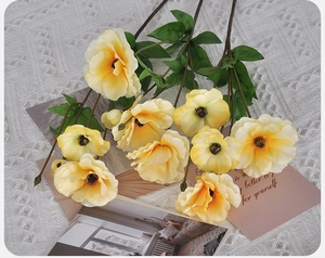 Detail of yellow silk poppies on white lace tablecloth with decorative postcard