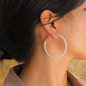 On-ear view of large C-shaped gold hoops with white pearls on a female model