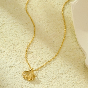 18K gold plated ginkgo leaf necklace with freshwater pearl pendant on beige stone background