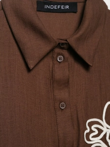 Detail of dark brown linen shirt featuring white floral embroidery and classic square collar