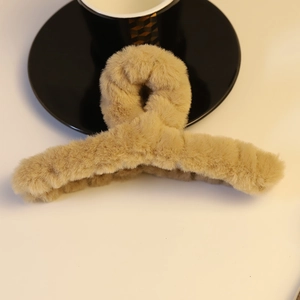 Detailaufnahme einer beigefarbenen Plüsch-Haarklammer mit gedrehtem Design auf Weiß
