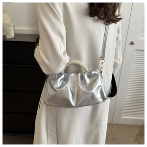 Silver pleated cloud handbag with pearl handle shown on a model in a minimal home setting
