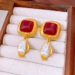 Macro detail of vintage gold hammer-textured earrings with red resin and baroque pearls