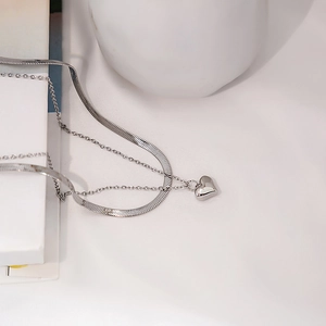 Detail of silver layered snake chain and delicate link necklace with heart pendant