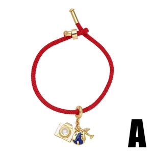 Red braided cord bracelet with gold camera, globe, and airplane charms on white background