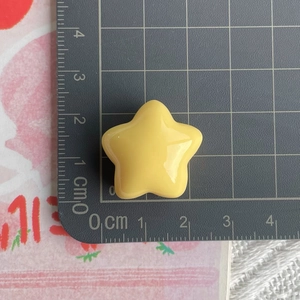Macro shot of 25mm glossy yellow resin star charm on a grid measurement scale mat