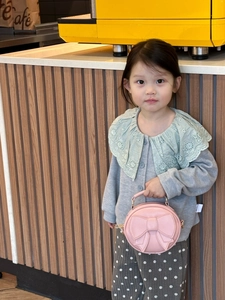 Pink round children handbag featuring a large bow and detachable shoulder strap detail