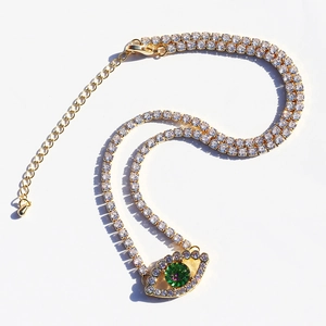 Macro detail of gold eye pendant with green zircon and clear rhinestone tennis chain