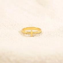 Detailed macro view of golden cross ring with pavé small diamonds on a warm textured surface