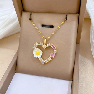 Nahaufnahme von goldenem Herzanhänger mit rosa Steinen und Gänseblümchen in einer Box