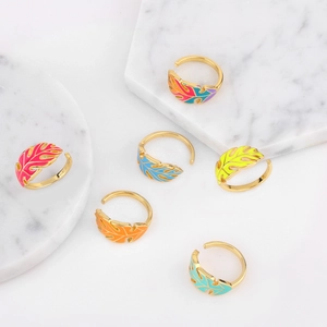 Detail of six gold-plated enamel leaf rings in vibrant colors on a marble background