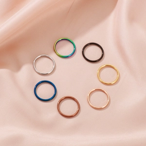 Minimalist stainless steel stackable bands in seven colors on a pink silk background
