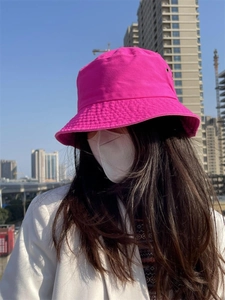 Close-up of pink cotton bucket hat with metal eyelets worn by a model in sunlight