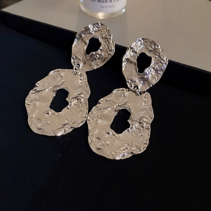 Macro shot of silver geometric earrings with irregular lava texture and metallic luster