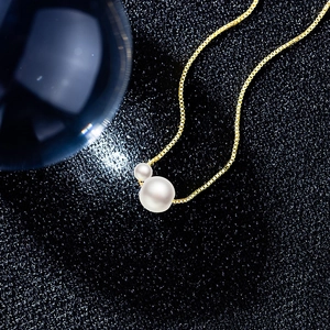 Detailed close-up of a gold box chain pearl necklace featuring two white pearls on dark background
