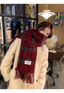Close-up of red plaid wool scarf with fringes worn by a model in a cozy cafe setting