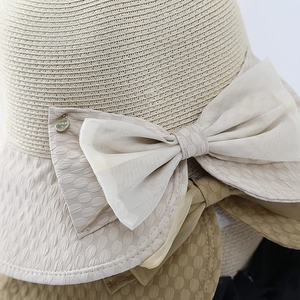 Détail d'un chapeau de paille avec un grand nœud en mesh et un logo doré rond