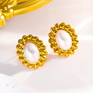 Twisted gold-plated earrings with white pearls and cat eye stones on a soft background