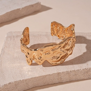 Detailed view of golden irregular wavy textured open bangle on a stone pedestal