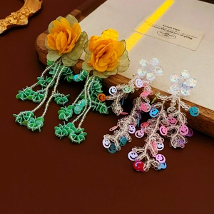 Détail de boucles d'oreilles fleur en tissu avec longs pompons perlés et paillettes