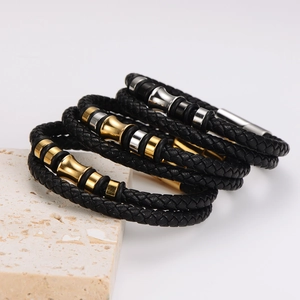 Juego de tres pulseras de cuero trenzado negro con detalles de tubos metálicos oro y plata