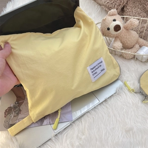 Yellow fabric laptop sleeve with white logo tag on soft white faux fur background