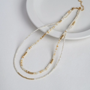 Double-layered beaded necklace with white seeds, shell discs and golden lobster clasp