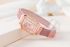 Detail of rose gold hexagonal watch with pink dial and magnetic mesh strap on white fabric